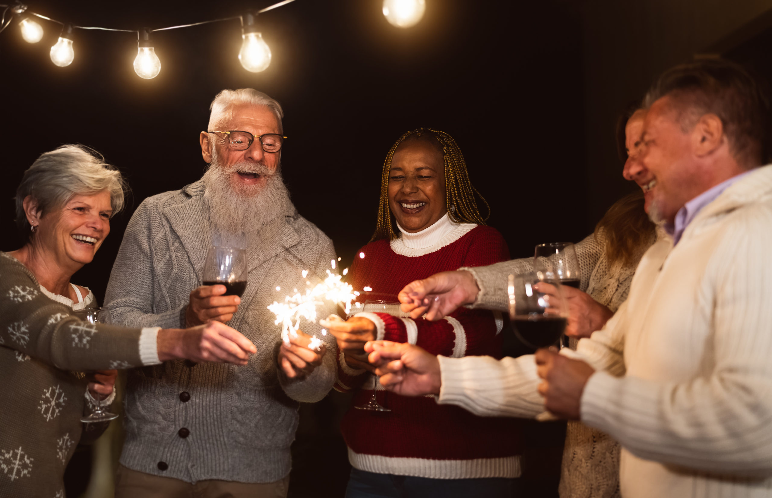 Happy seniors having fun celebrating holidays drinking wine and holding sparklers fireworks