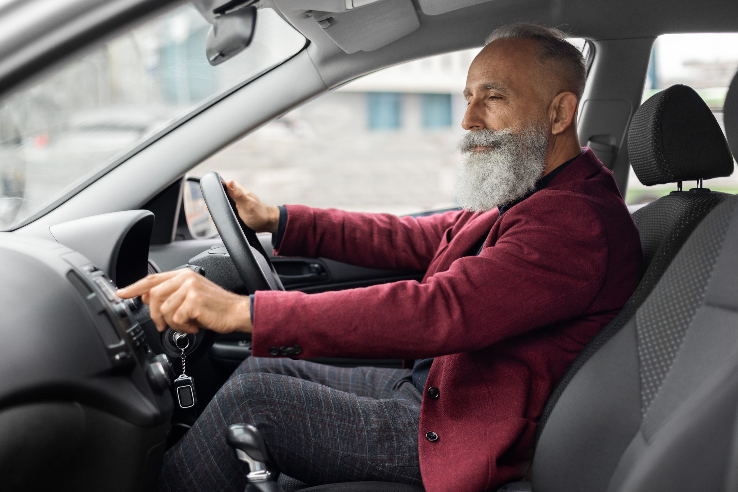 Senior man driver turning on music in car before moving